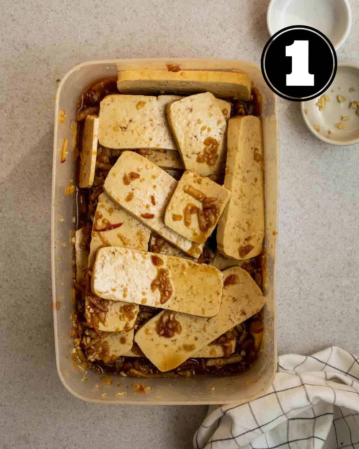 Marinating tofu slices in a clear container.