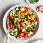 A plate of cucumber tomato corn salad with a fork beside.