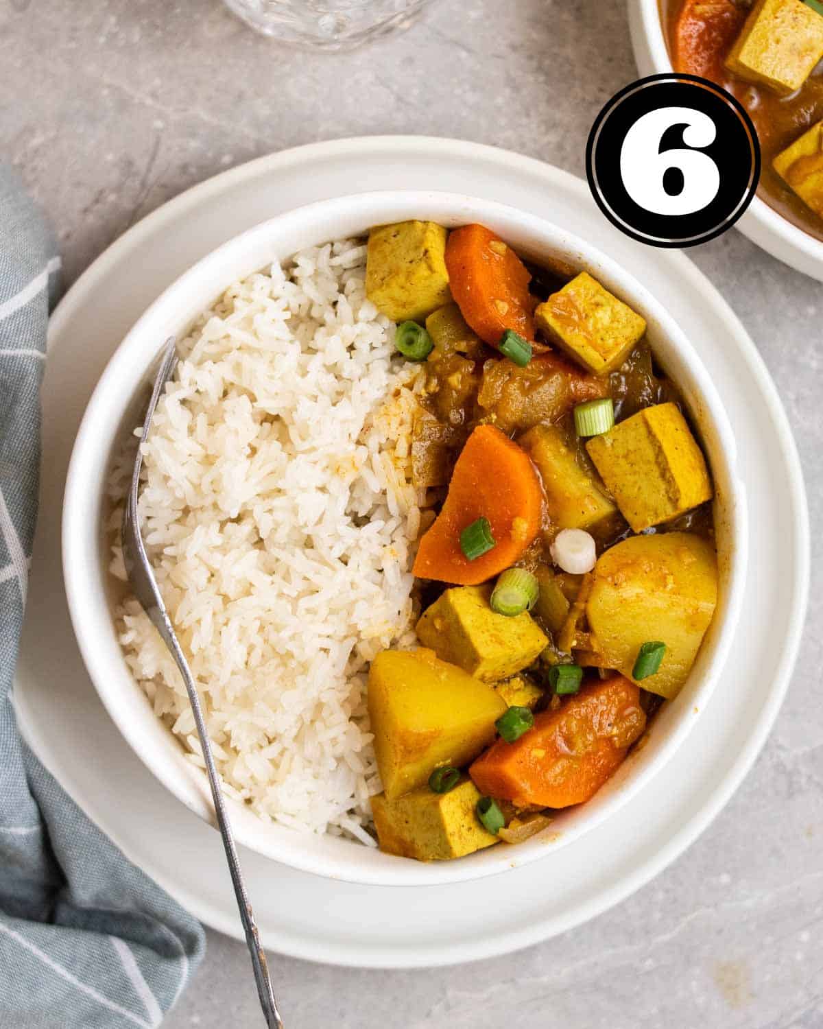 A bowl of Japanese curry served with rice on a plate with a spoon beisde.