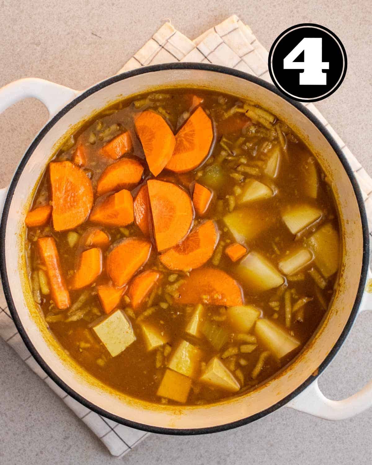 Uncooked carrot and potatoes in a pot of curry.