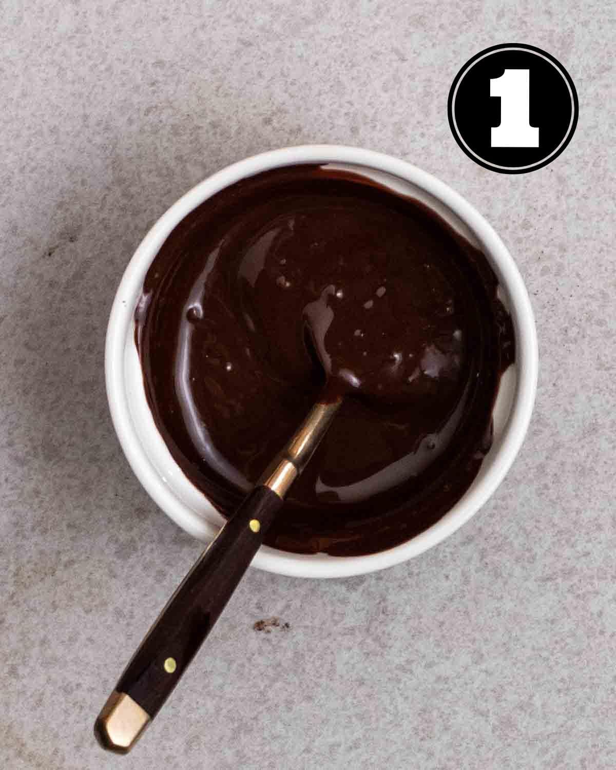 Melted chocolate in a ramekin with a teaspoon beside.