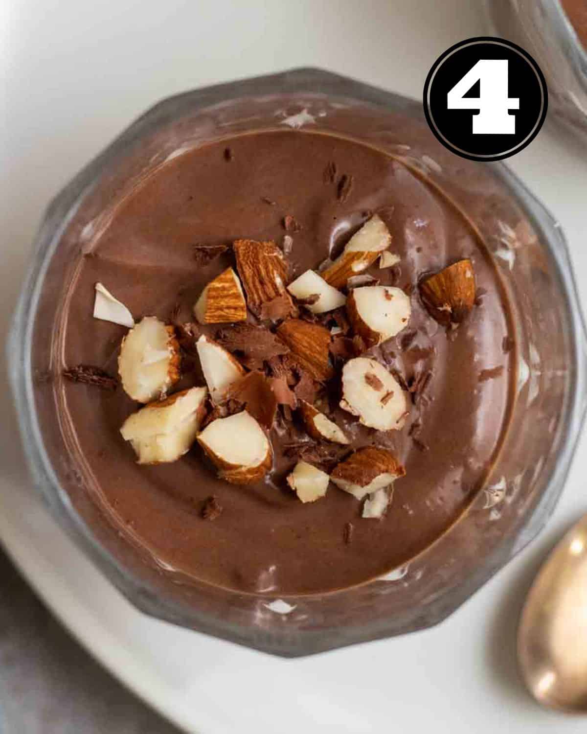 A jar of tofu chocolate pudding topped with chopped almonds with a spoon beside.