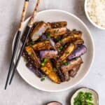 A plate of eggplant served with chopsticks with rice and green onion beside.