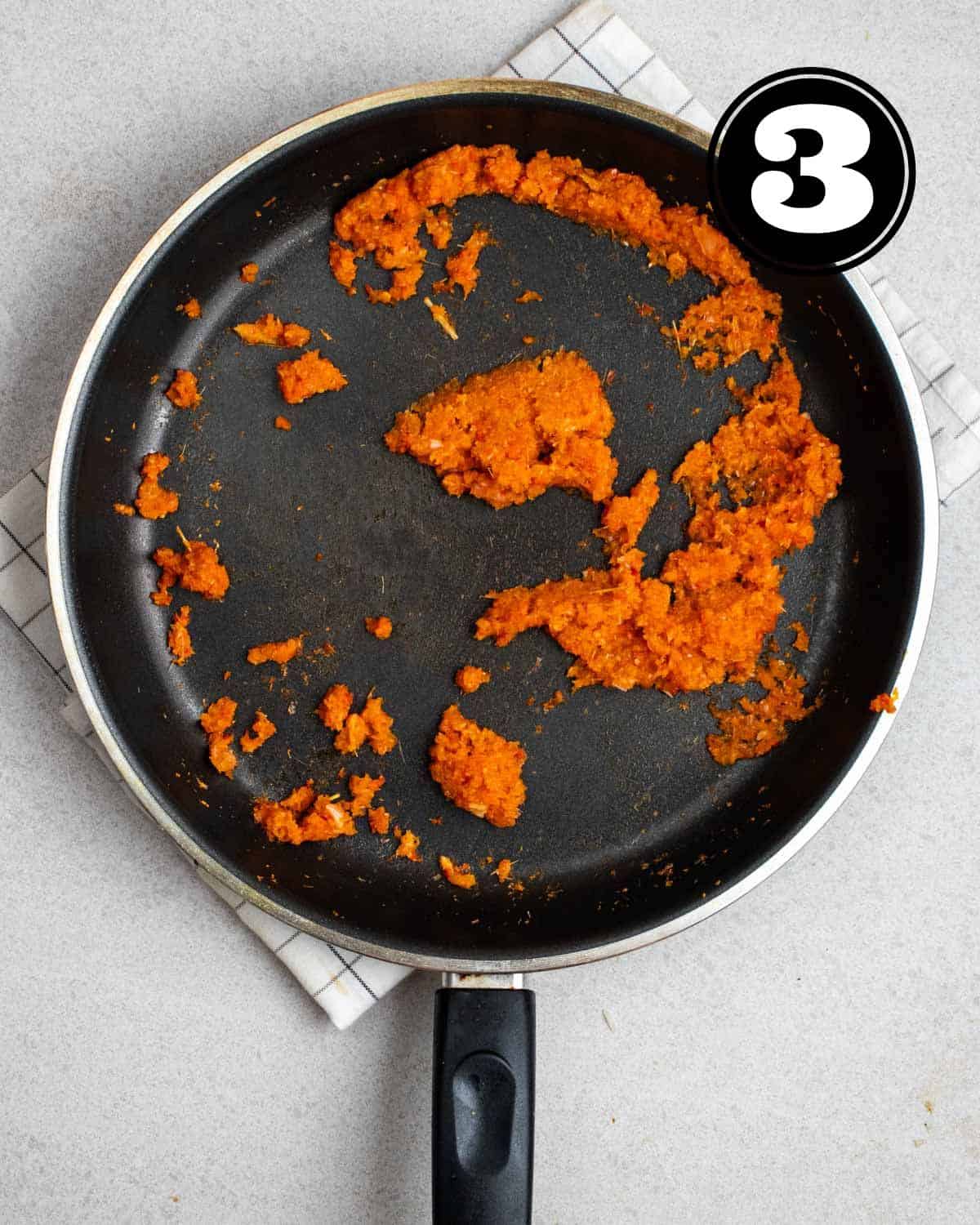 Fried sambal paste in a non-stick pan on a white folded teacloth.