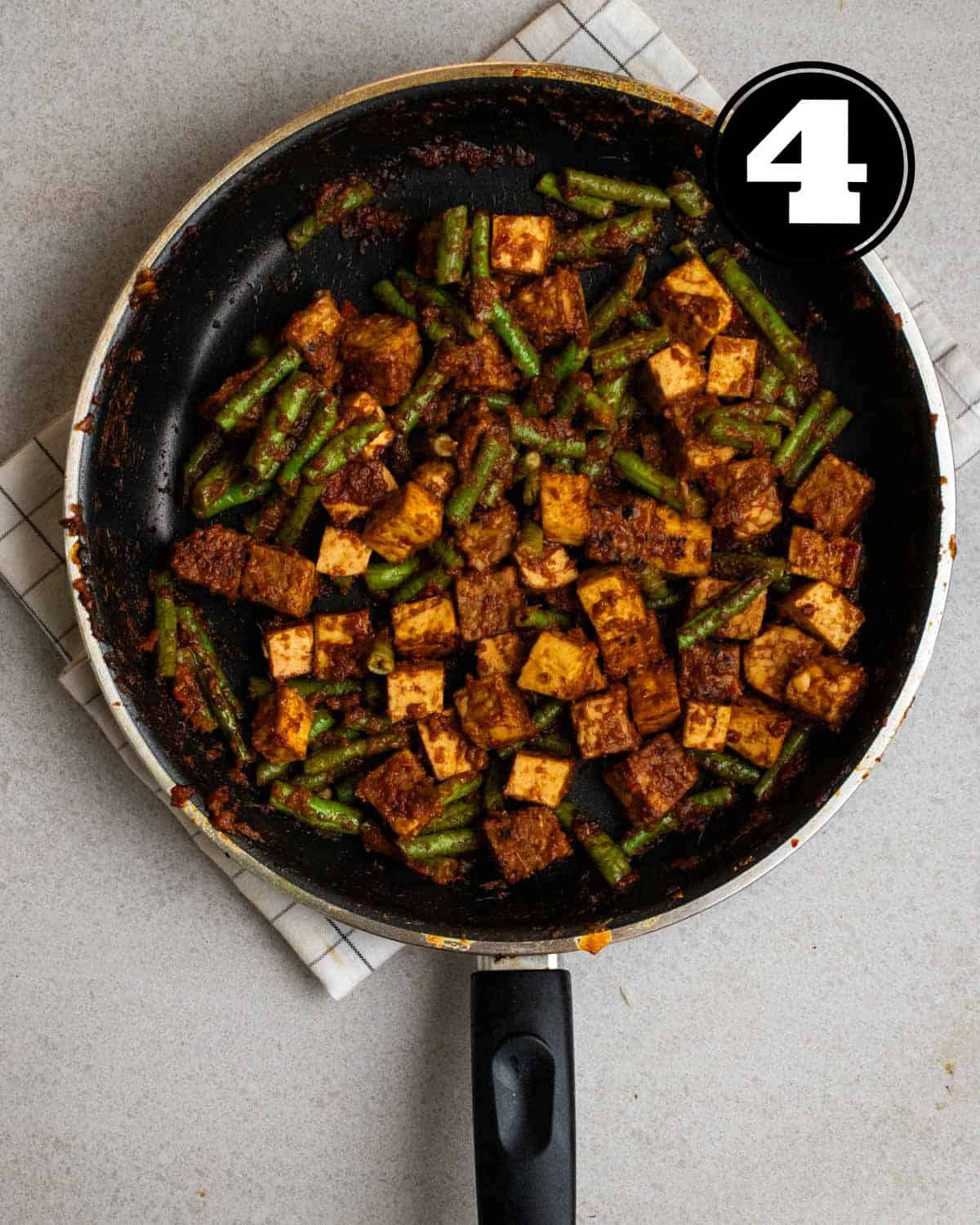Sambal tempeh in a non-stick pan on a white folded teacloth.