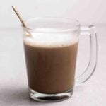 A glass of soy latte with a teaspoon beside.