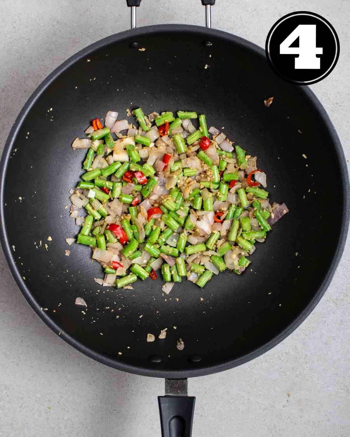Cooked French beans, onion, chilies, and garlic in a wok.