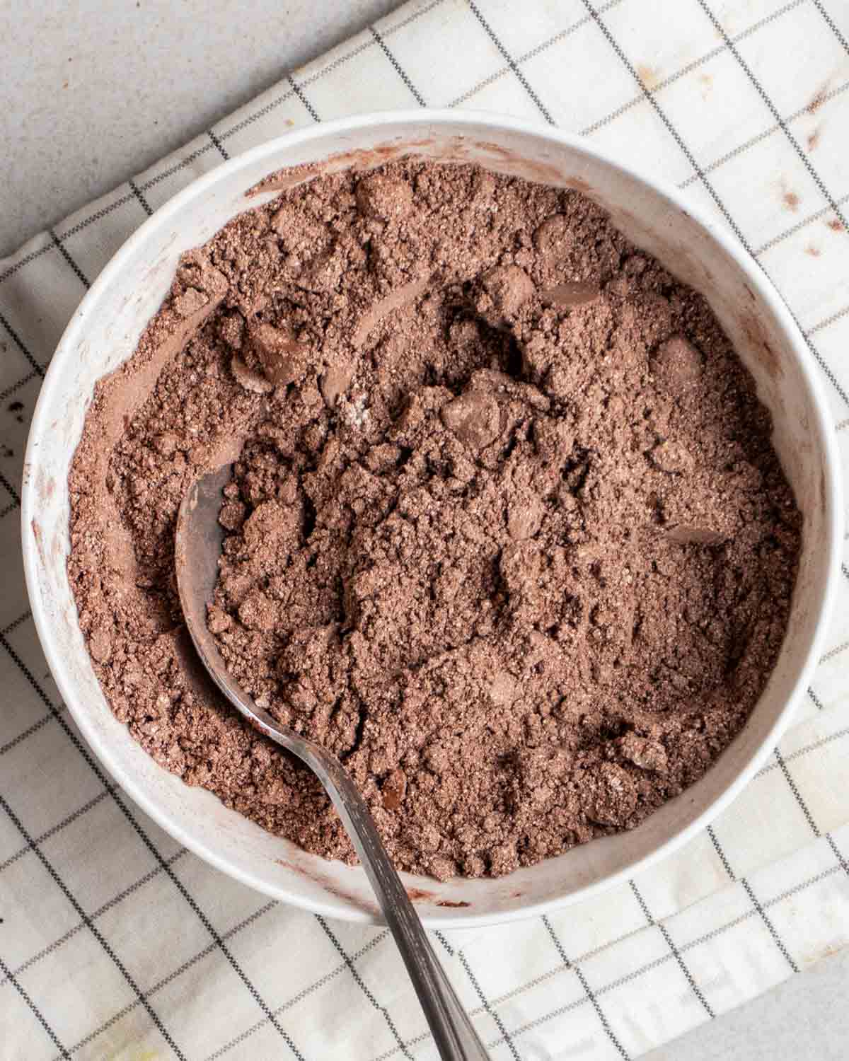 Dry ingredients for brownies in a bowl with a spoon beside on a folded white teacloth.