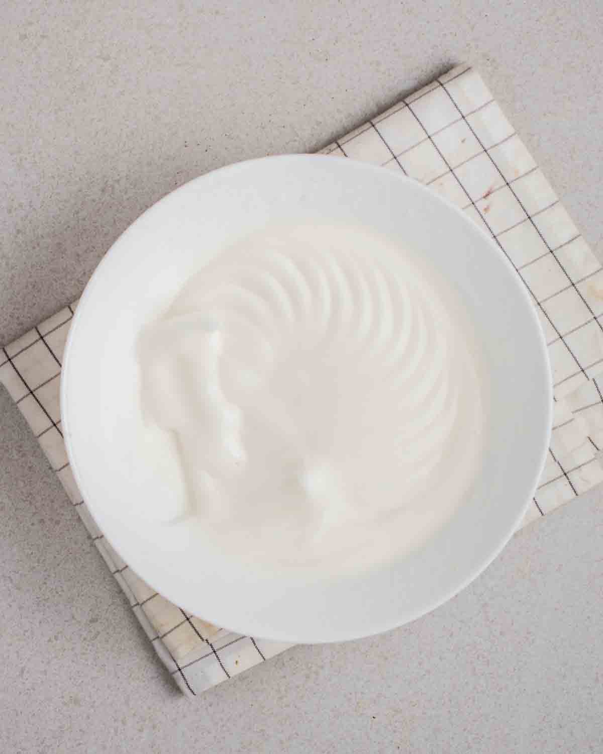 Whisked aquafaba in a bowl on a white checkered teacloth.