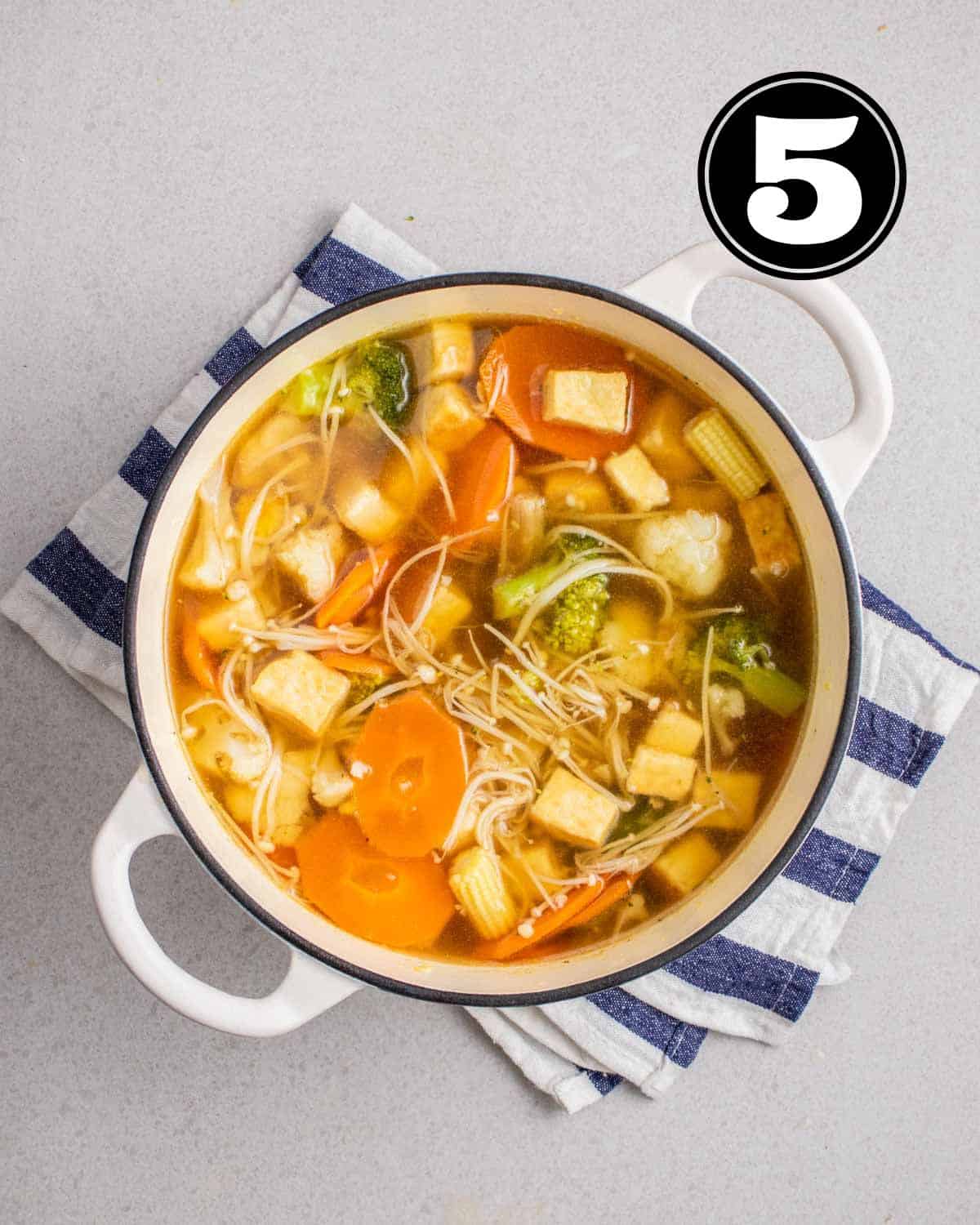 Chinese vegetable soup in a white Dutch oven on a folded blue and white teacloth.