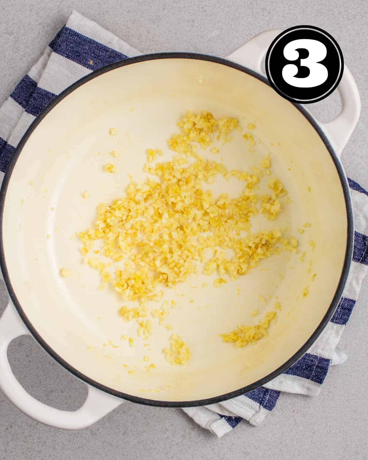Cooked garlic and ginger in a white Dutch oven on a white and blue striped teacloth.