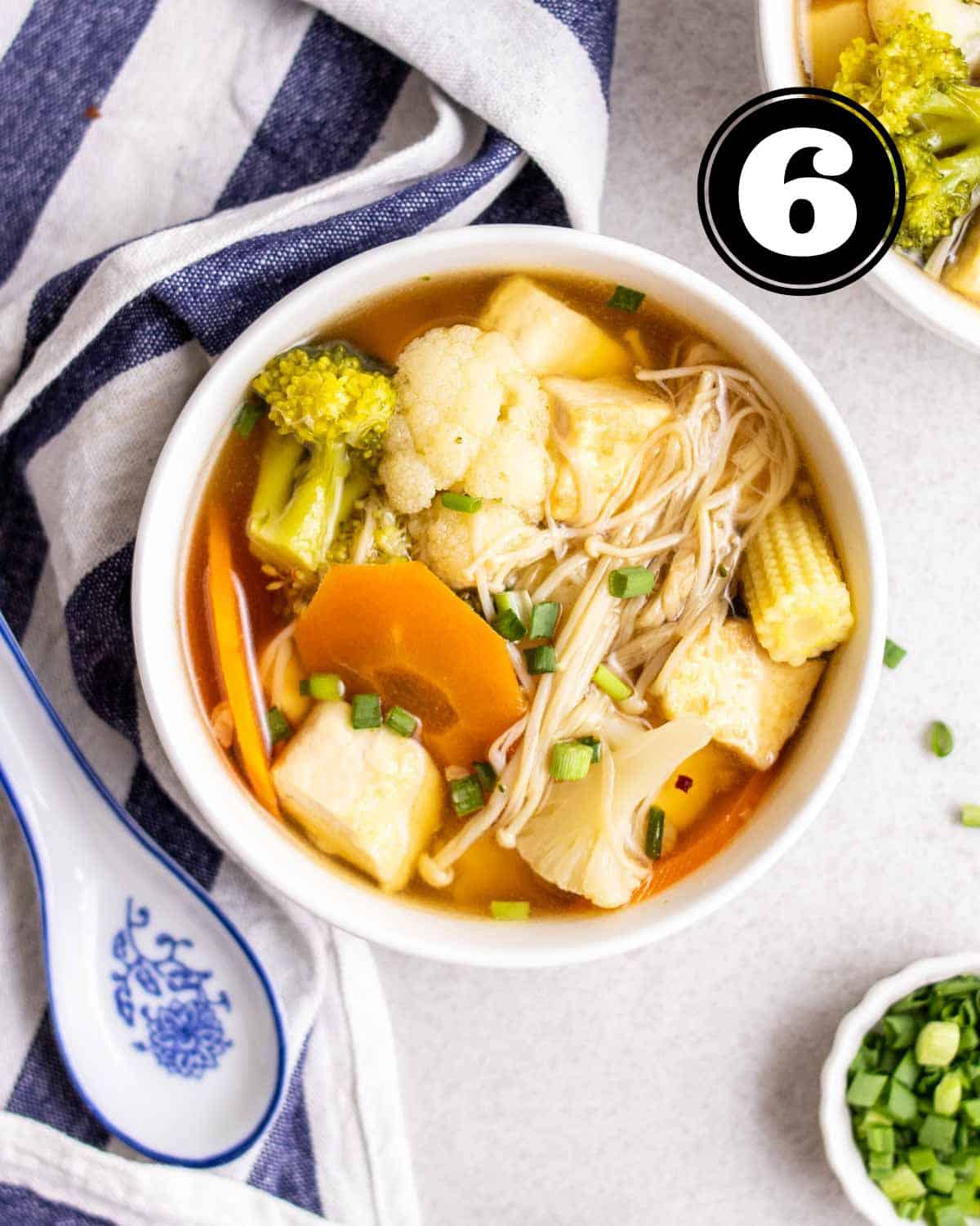 A bowl of Chinese vegetable soup served with a ceramic spoon beside.