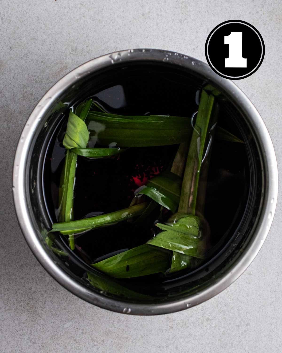 Uncooked black glutinous rice, pandan leave knots, and water in a pot.