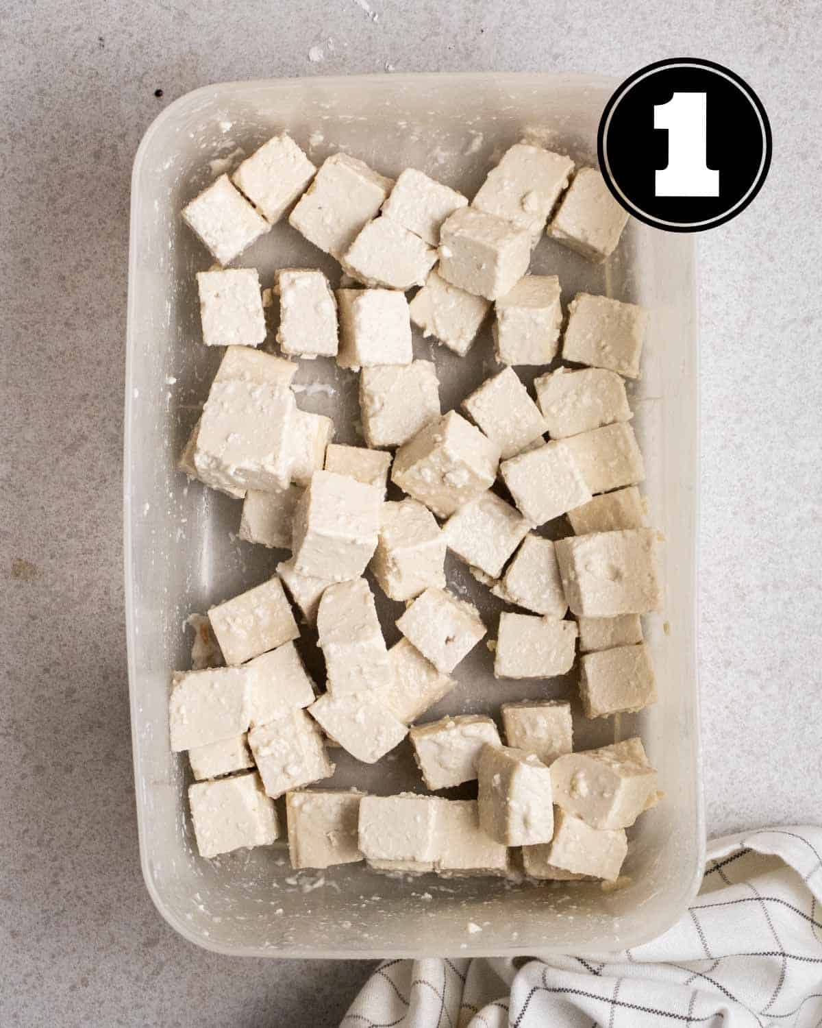 Coated tofu cubes in a square container with a white checkered teacloth beside.