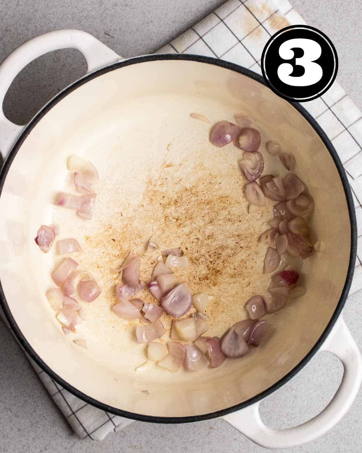 Cooked onion in a Dutch oven on a folded white teacloth.