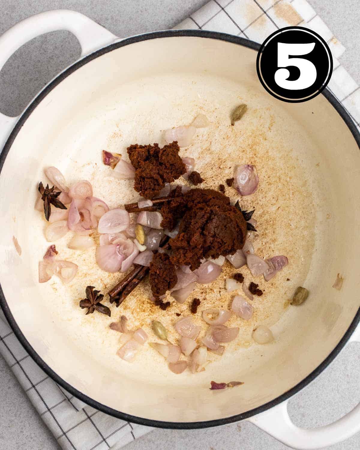 Adding curry paste to a pot of cooked onion and spices.