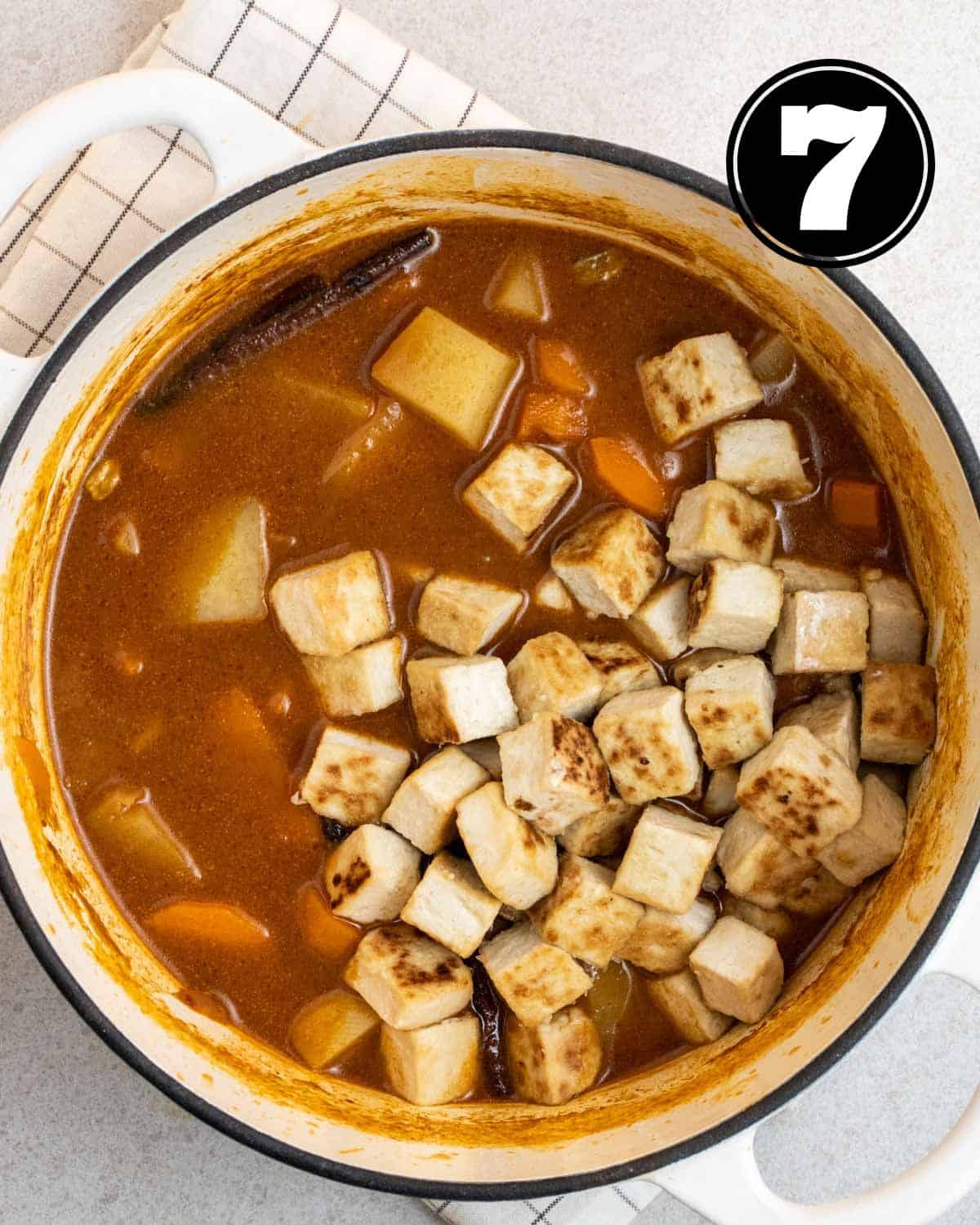 Adding pan-fried tofu to a pot of Massaman curry in a white Dutch oven.