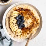 A bowl of millet porridge served with spoon with a cup of coffee beside.