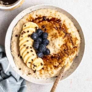 A bowl of millet porridge served with spoon with a cup of coffee beside.