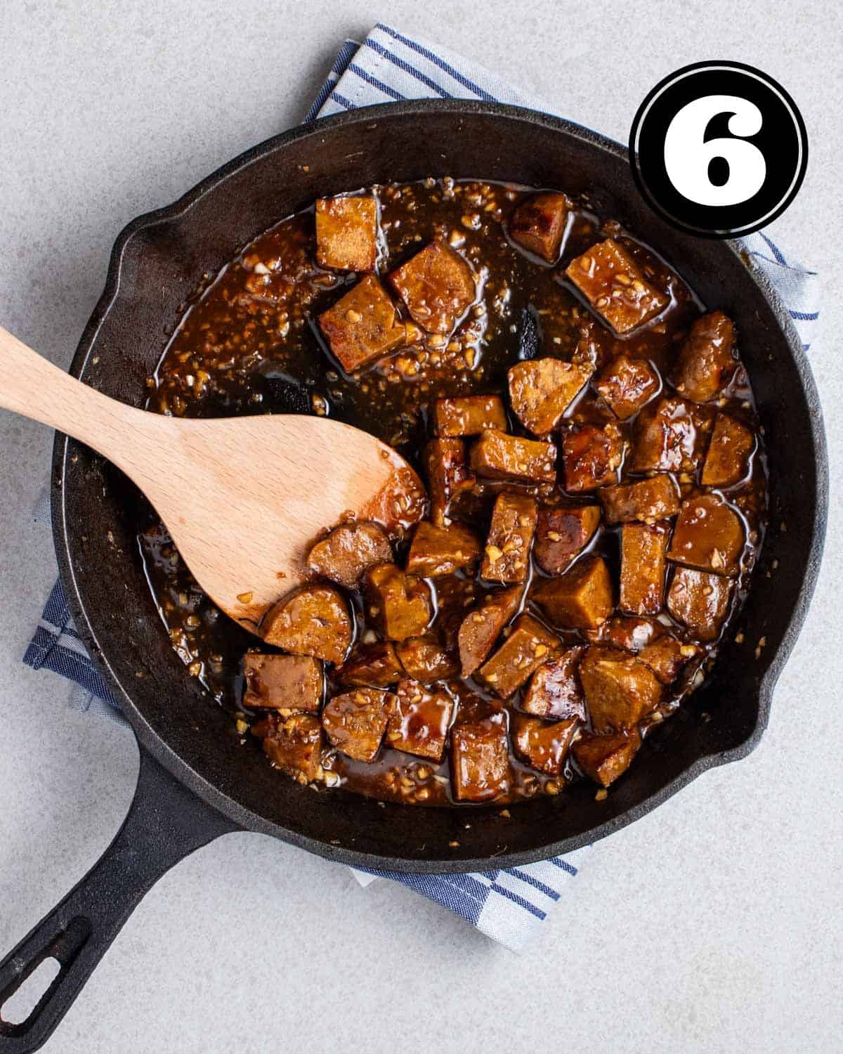 Vegan teriyaki chicken in a cast iron skillet with a wooden spatula beside.