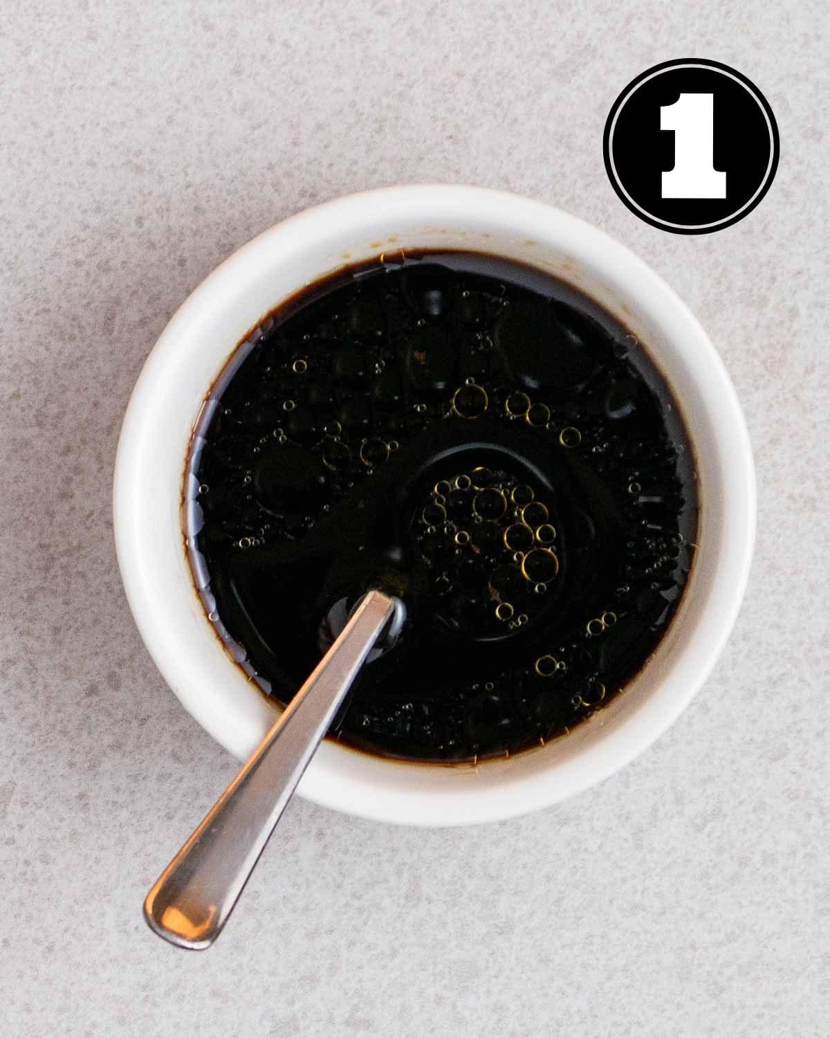 Sauce for teriyaki chicken in a white ramekin with a teaspoon beside.