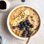 A bowl of barley porridge with maple syrup and blueberries beside.