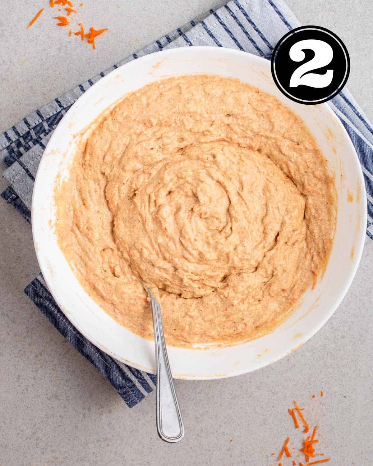 Batter for applesauce carrot muffins in a white bowl with a spoon beside.