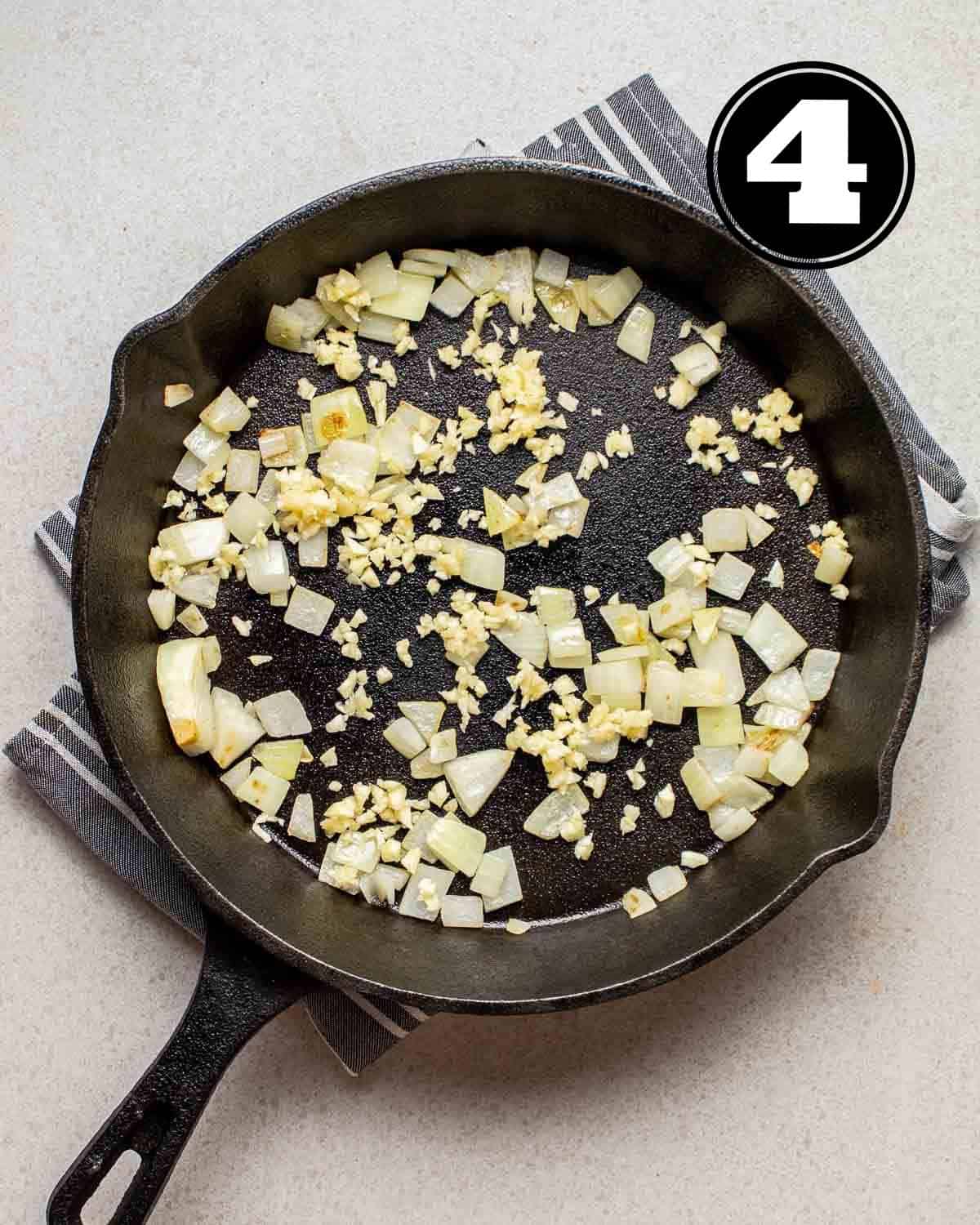 Cooked garlic and onion in a skillet on a folded blue striped teacloth.