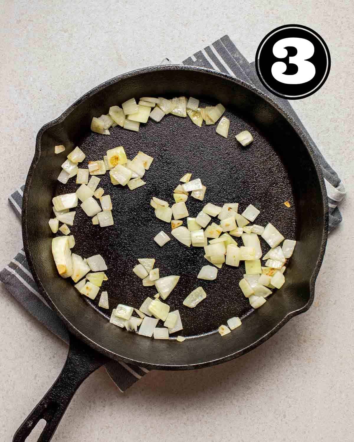 Cooked onion in a cast iron skillet on a blue and white folded teacloth.