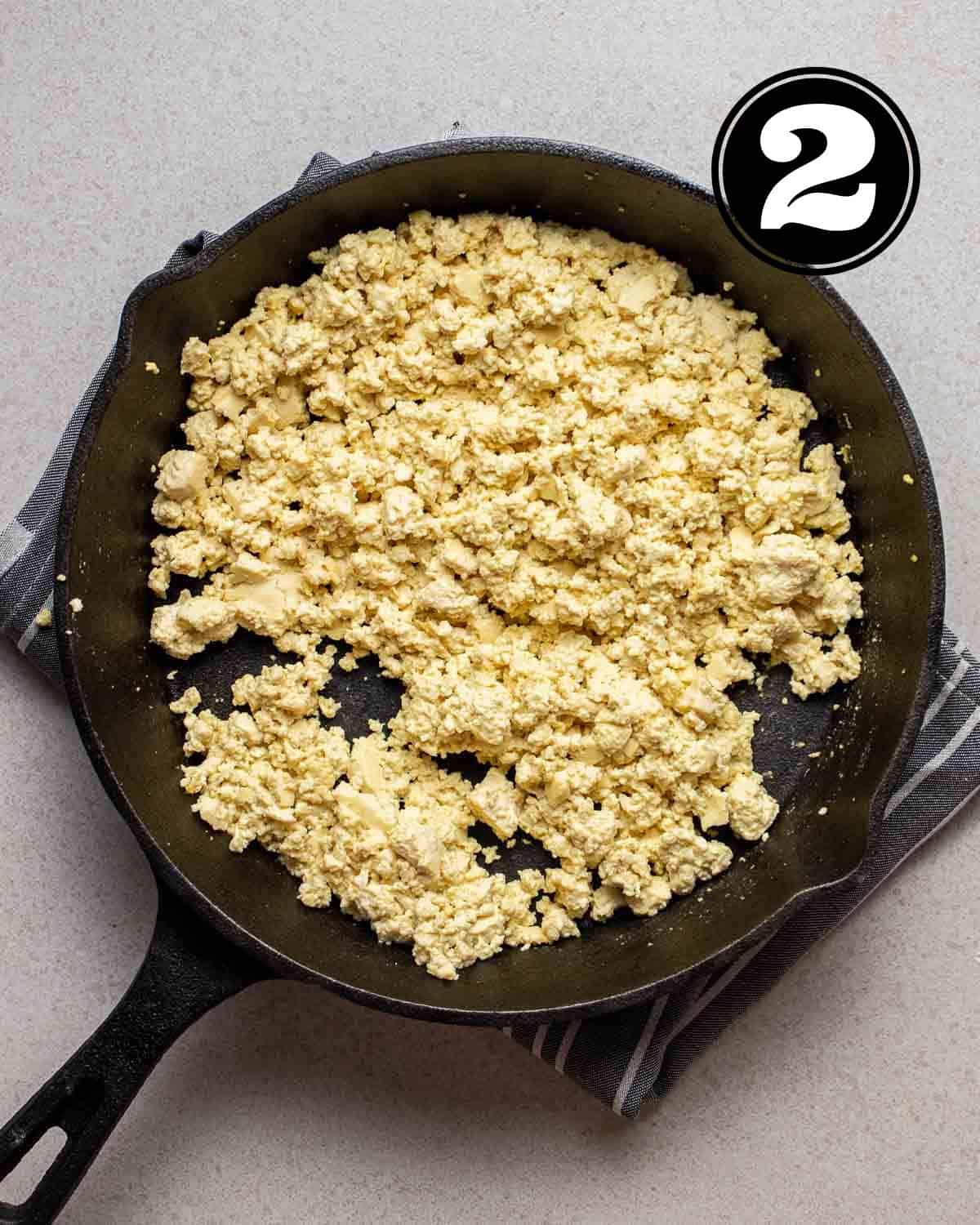 Cooked tofu scramble in a cast iron skillet on a folded white and blue teacloth.