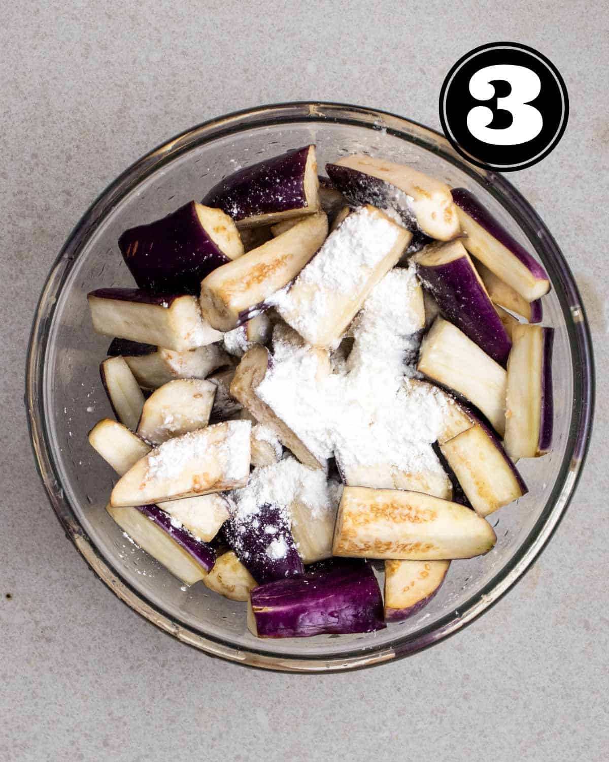 Adding cornstarch to eggplant slices in a glass bowl.