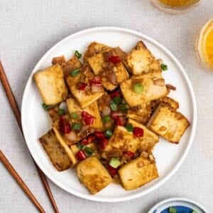 A plate of lemongrass tofu served with chopsticks and 2 glasses of tea.