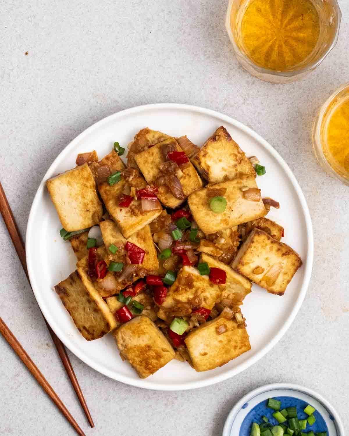 A plate of lemongrass tofu served with chopsticks and 2 glasses of tea beside.