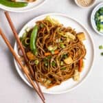 A plate of stir-fry noodles on a plate served with a pair of chopsticks.