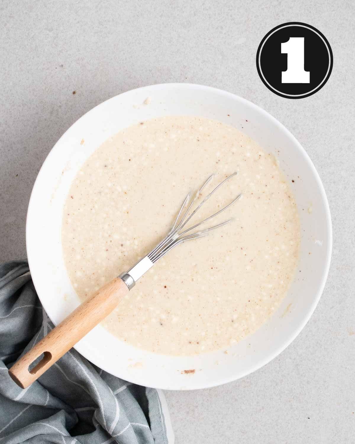 Crepe batter in a white bowl with a balloon whisk beside.