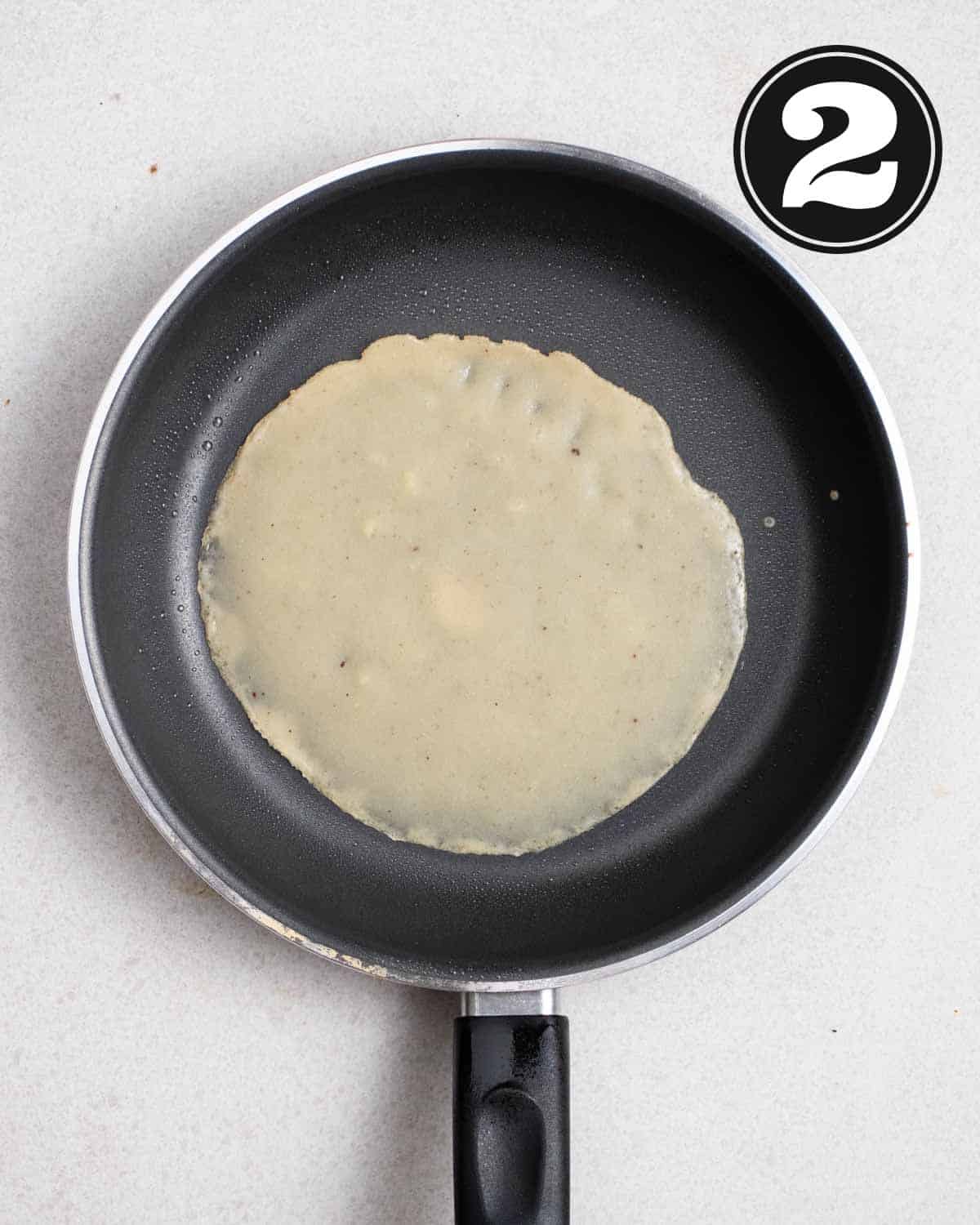 A partially cooked crepes in a non-stick pan.
