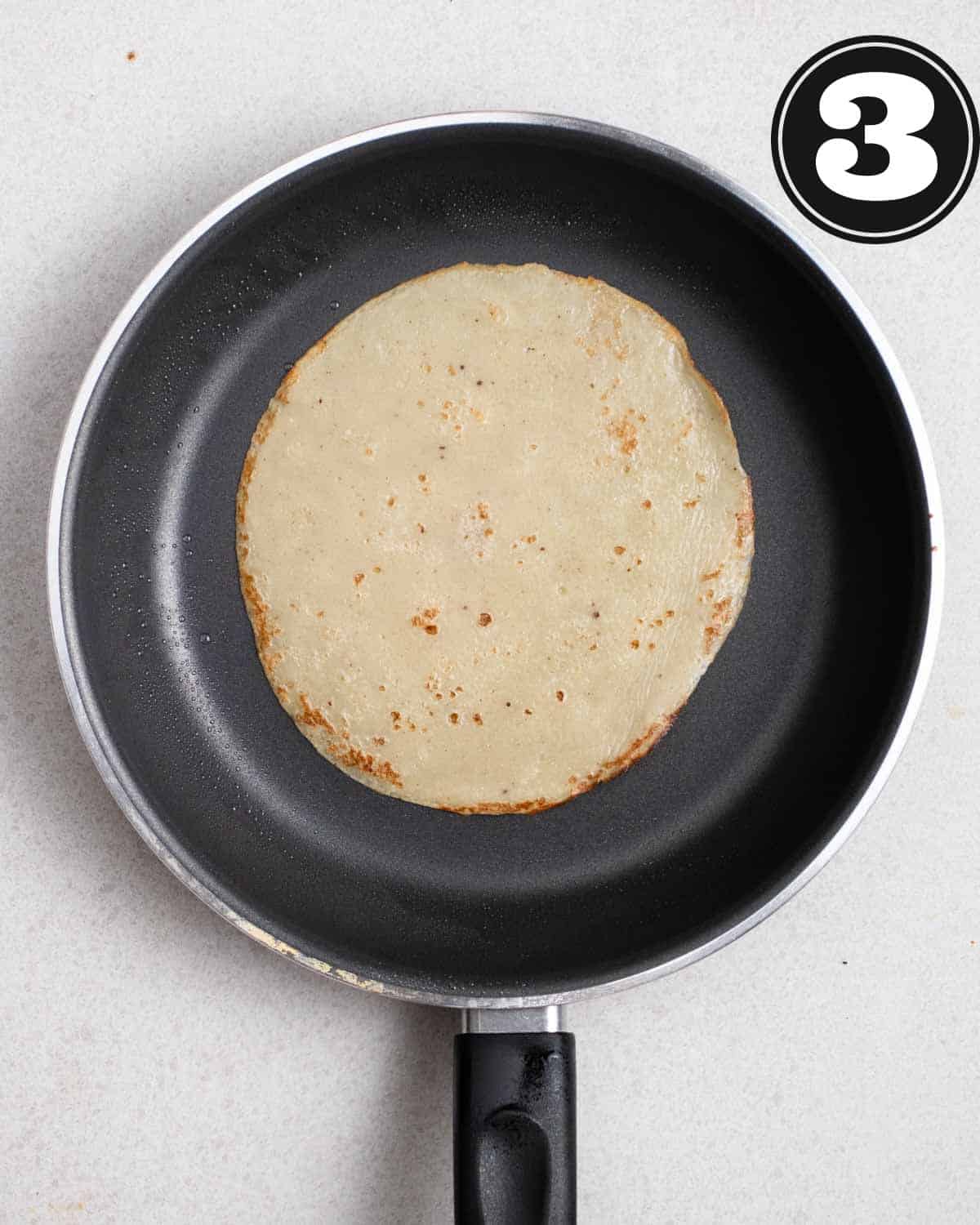 A cooked crepe in a non-stick pan.