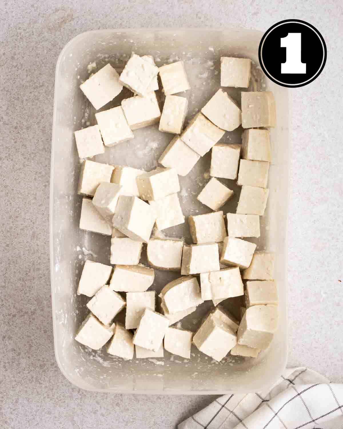Tofu coated in cornstarch in a rectangular transparent container.