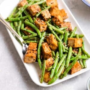 A plate of green beans tofu served with spoon topped with sesame seeds.