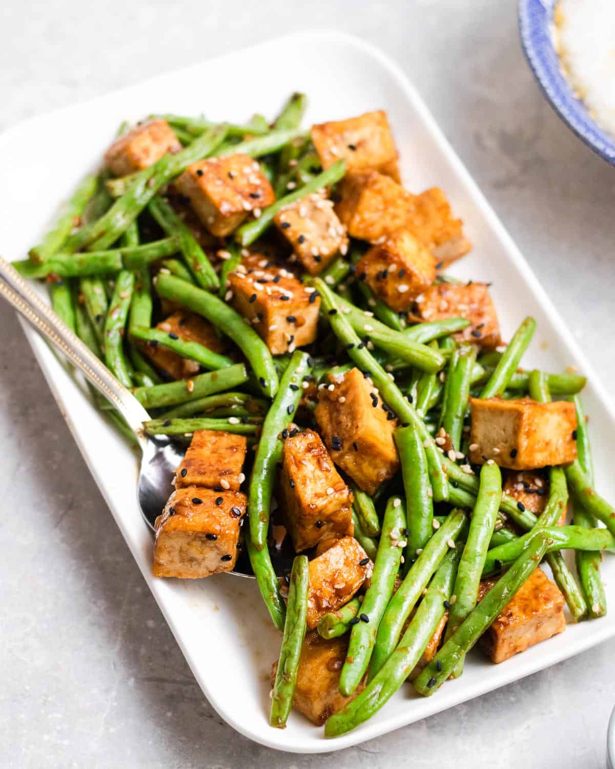 A plate of green beans tofu with a bowl of congee in the background.