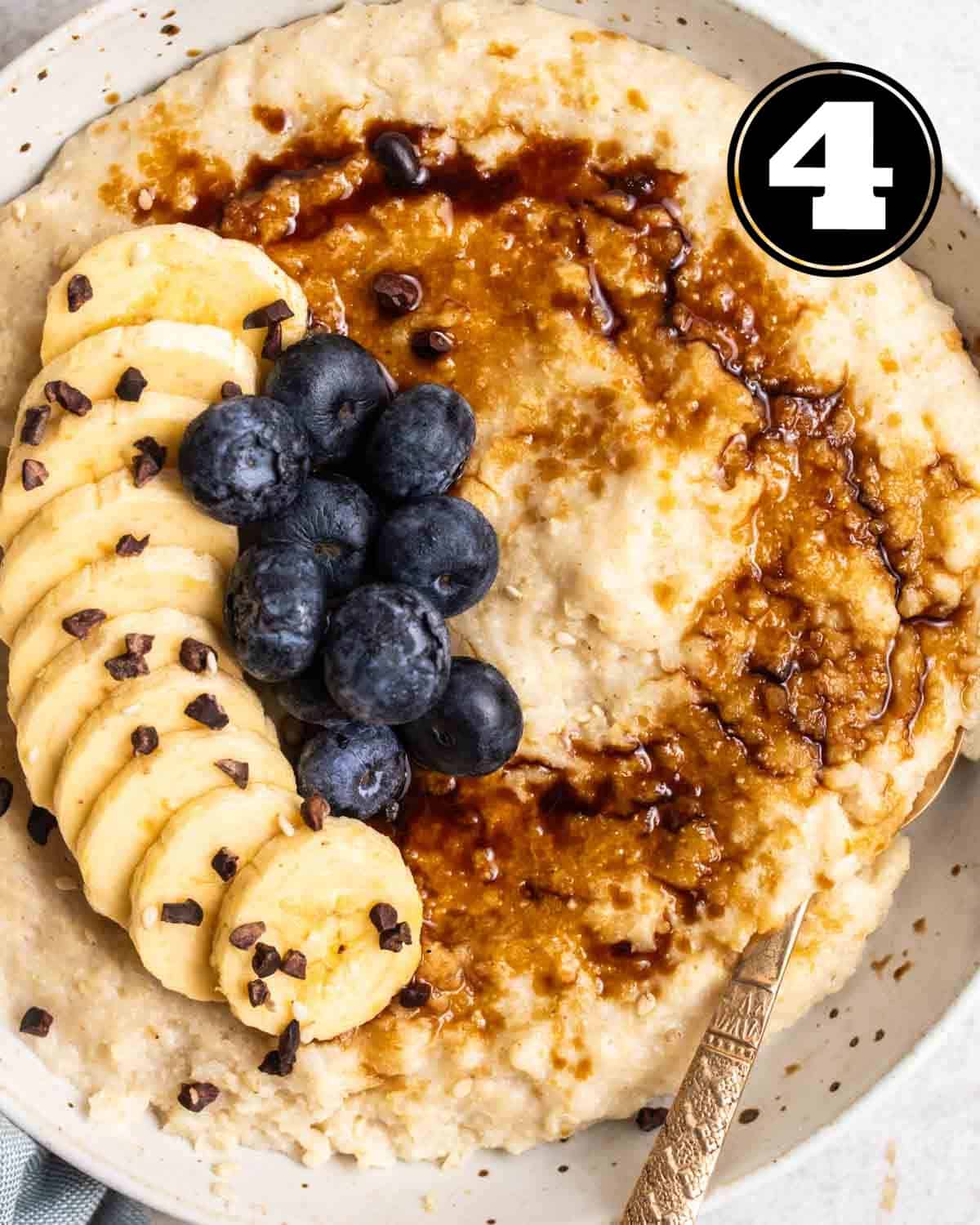 Bowl of millet porridge served with spoon topped with banana slices, cacao nibs, and blueberries.