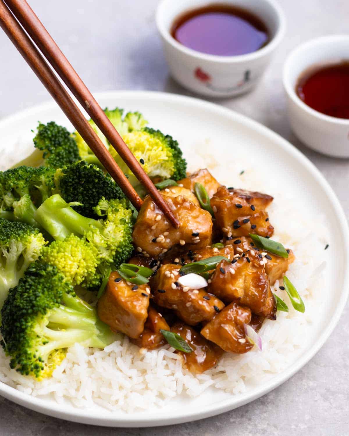 Holding a piece of tofu from a plate with 2 cups of tea in the background.