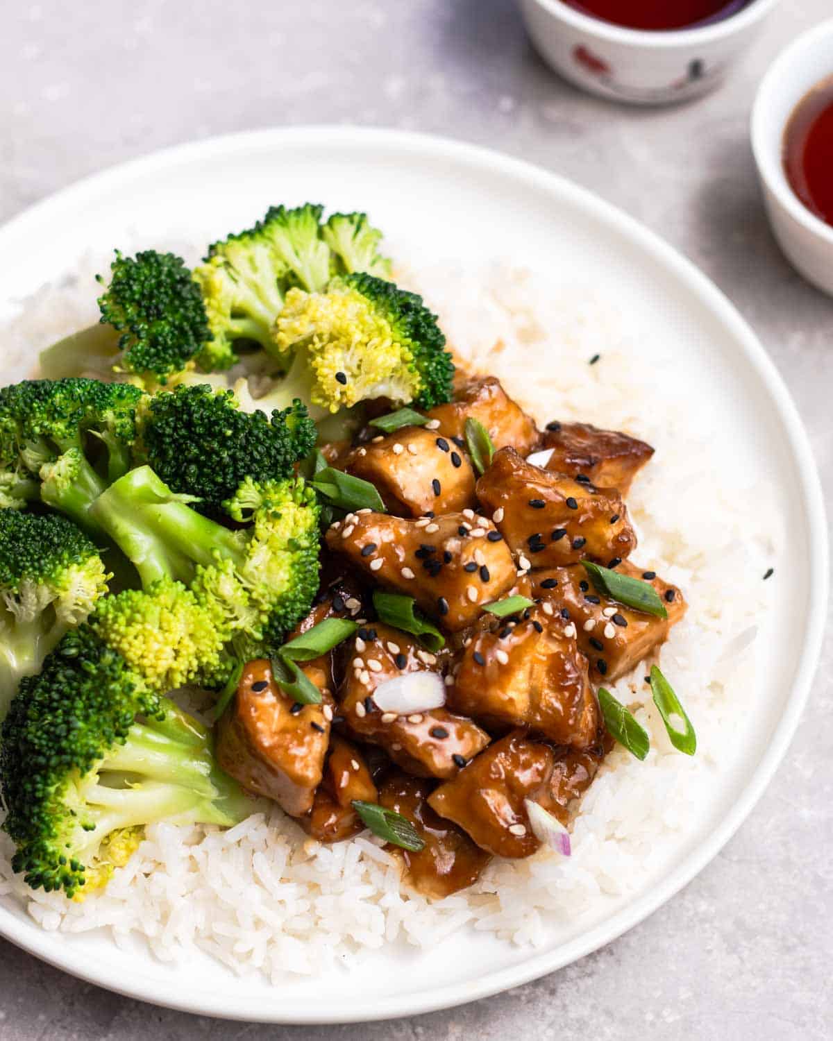Teriyaki tofu and broccoli served on rice with 2 cups of tea in the background.