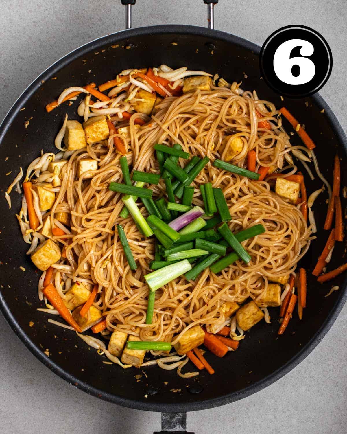 Adding green onion to a wok of cooked pad Thai.