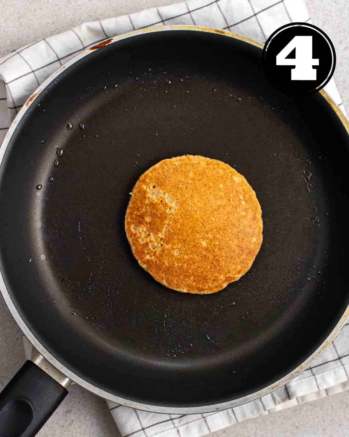 Cooked pancake in a non-stick pan on a white folded teacloth.