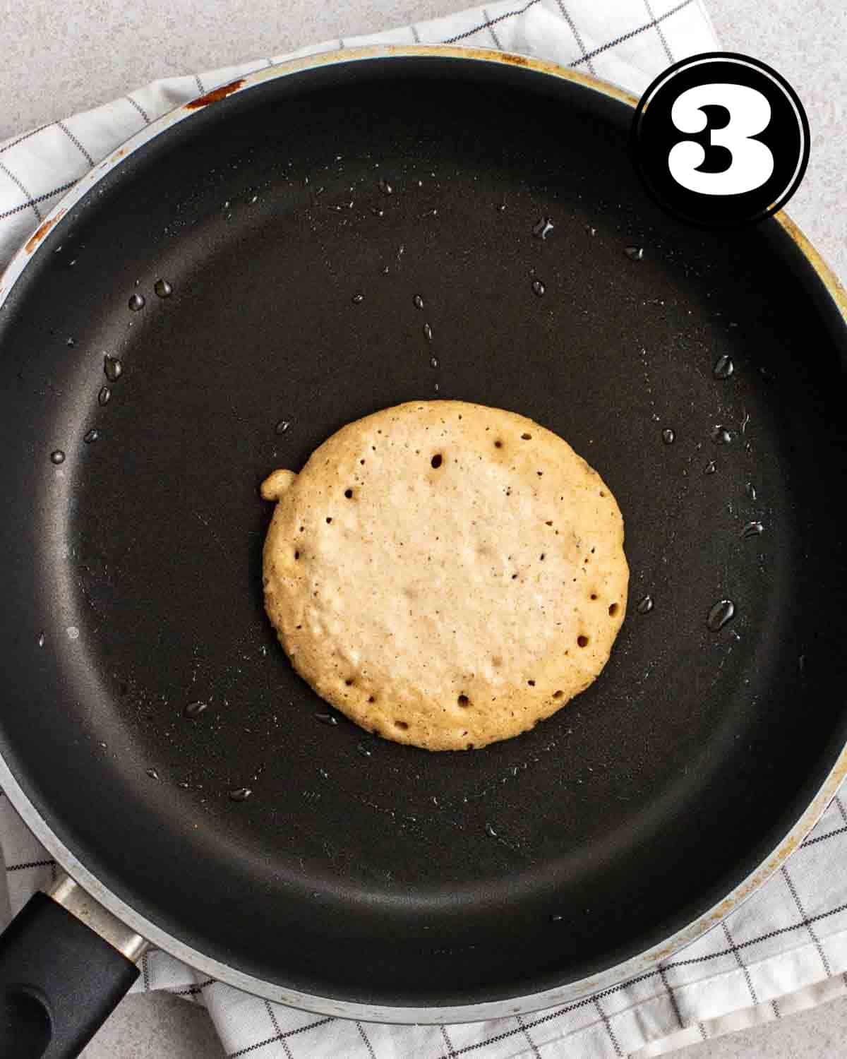Partially cooked pancake on a non-stick pan.