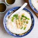 A bowl of congee served with spoon with 2 cups of tea beside.