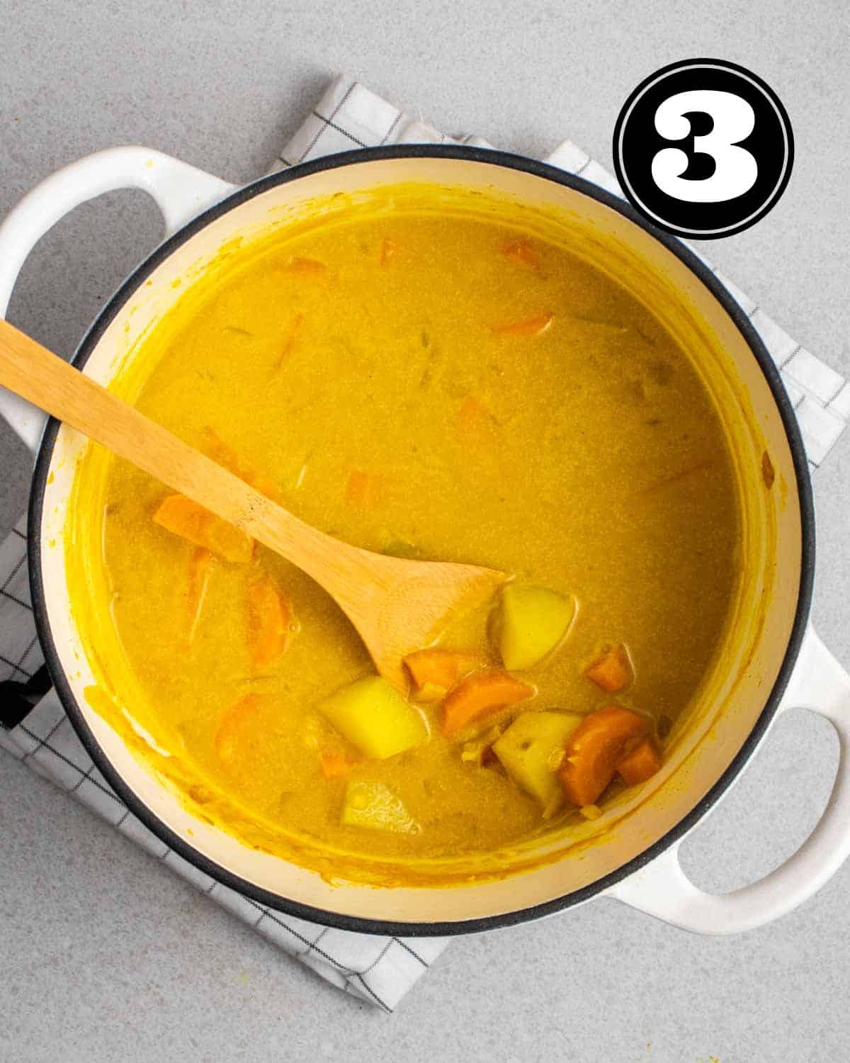 Carrot and potato in curry sauce with a wooden spatula beside.