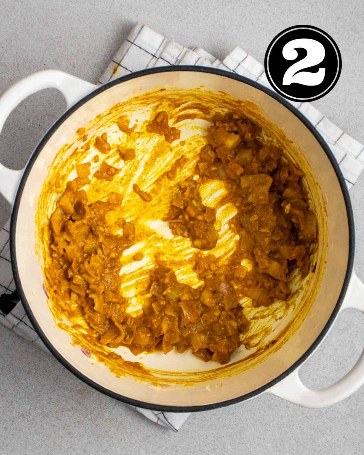 Cooked onion, garlic, and curry paste in a white Dutch oven on a white folded teacloth.