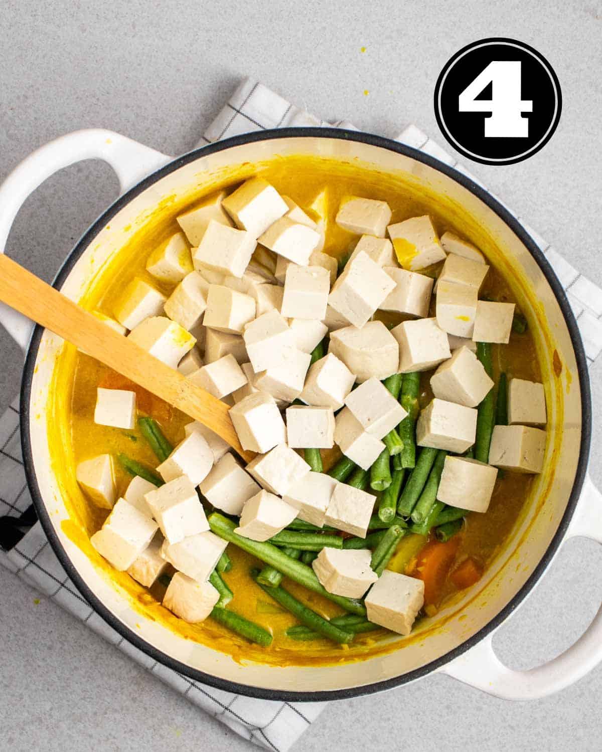 Adding tofu cubes and green onion to a pot of curry.